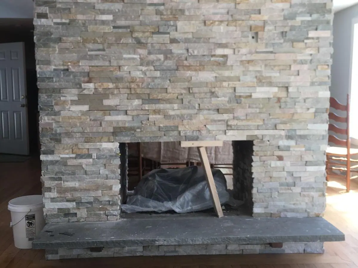 The same fireplace refaced in natural stacked stone veneer with a squared opening and a thick bluestone hearth