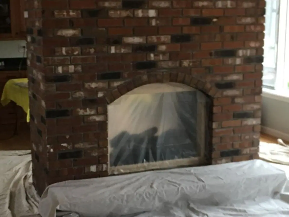 Two-sided red brick fireplace with an arched opening, floor covered with drop cloths before the work