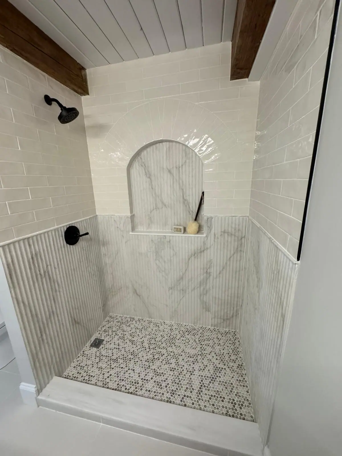 Shower with an arched niche, fluted marble-look wainscot and a black and white mosaic floor