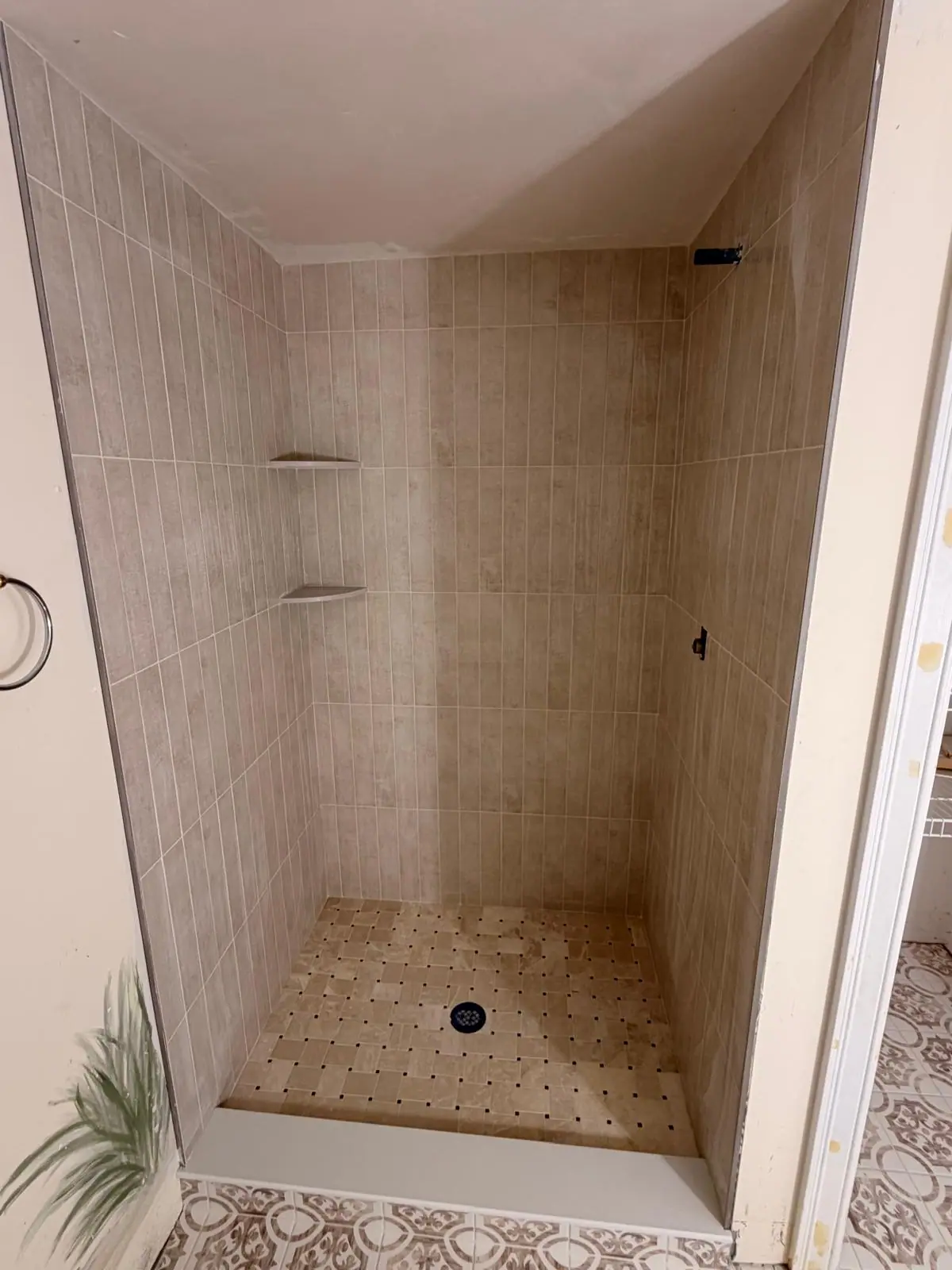 Beige tile shower with corner shelves and a mosaic floor
