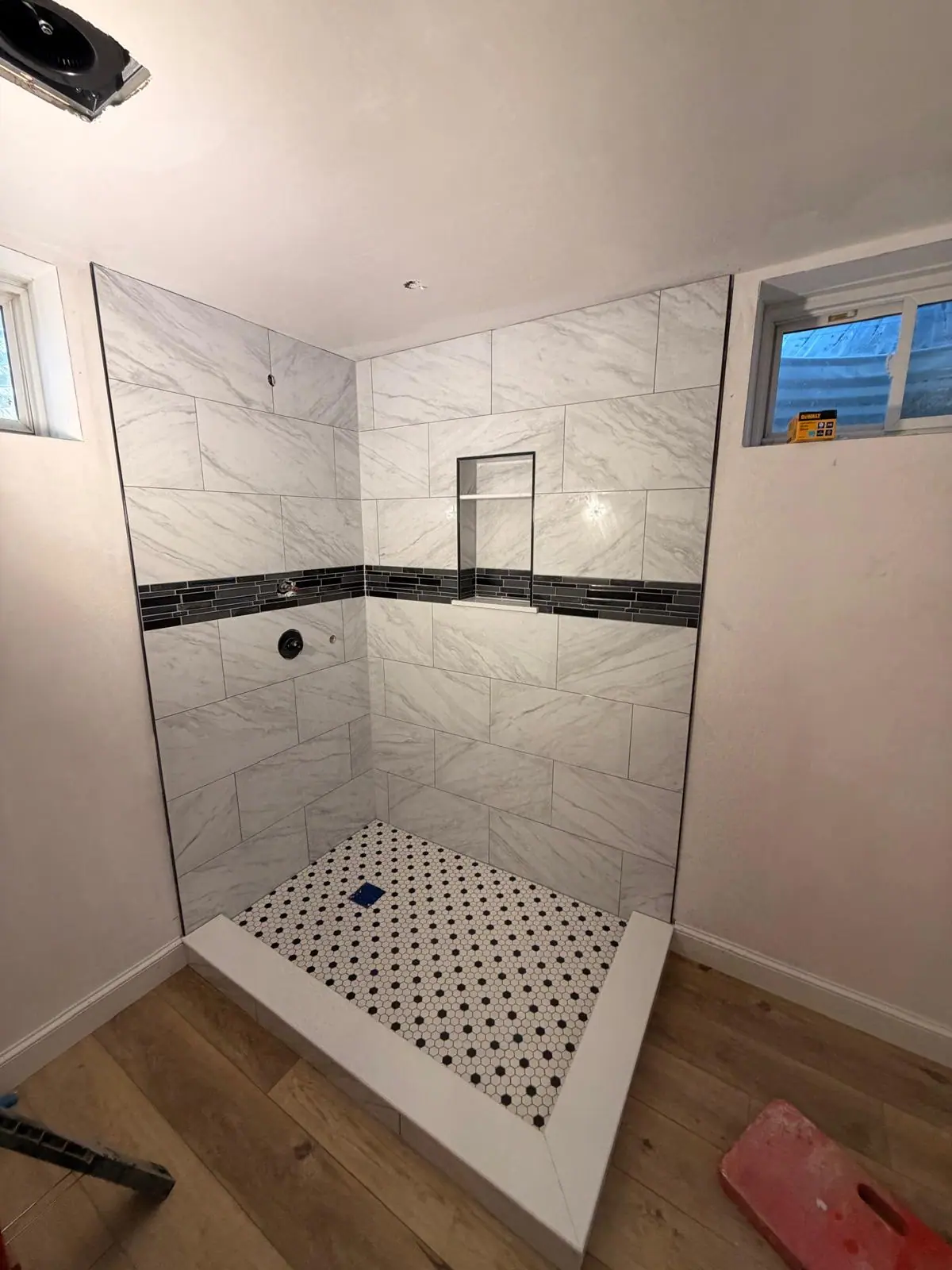 Marble-look shower with a black mosaic accent band, a niche and a black and white dot floor