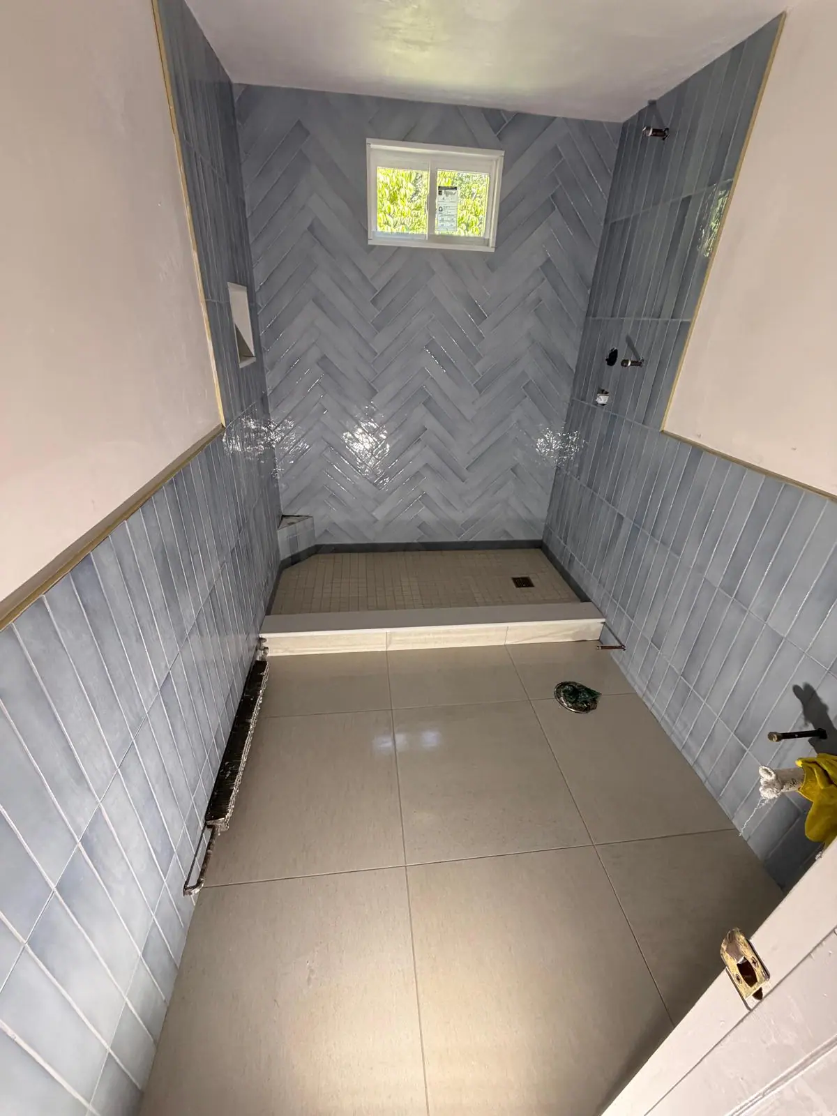 Bathroom with light blue tile walls, a herringbone shower wall and a large-format floor