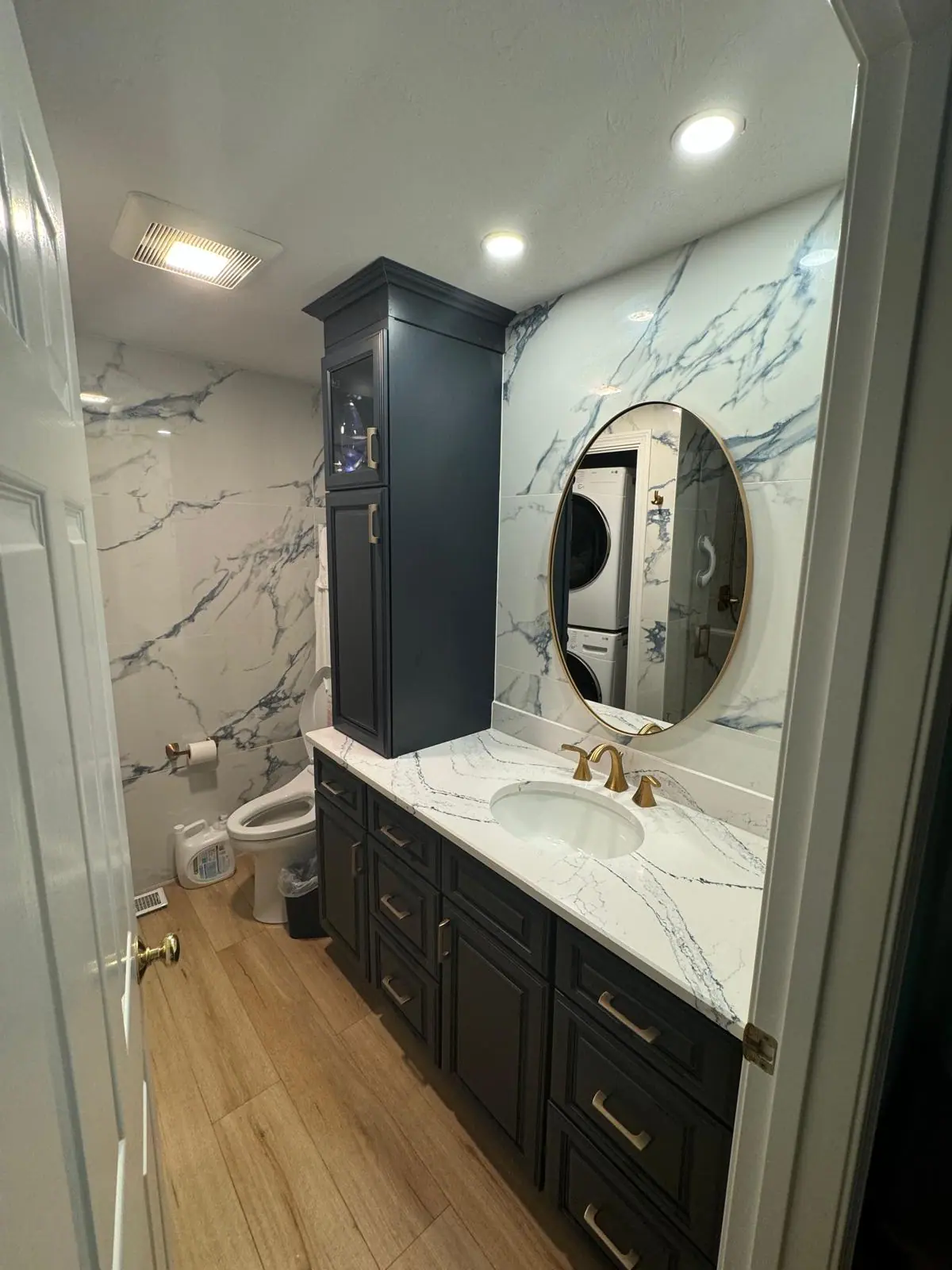Bathroom with blue-veined marble-look wall tile, a navy vanity with gold hardware and a round mirror