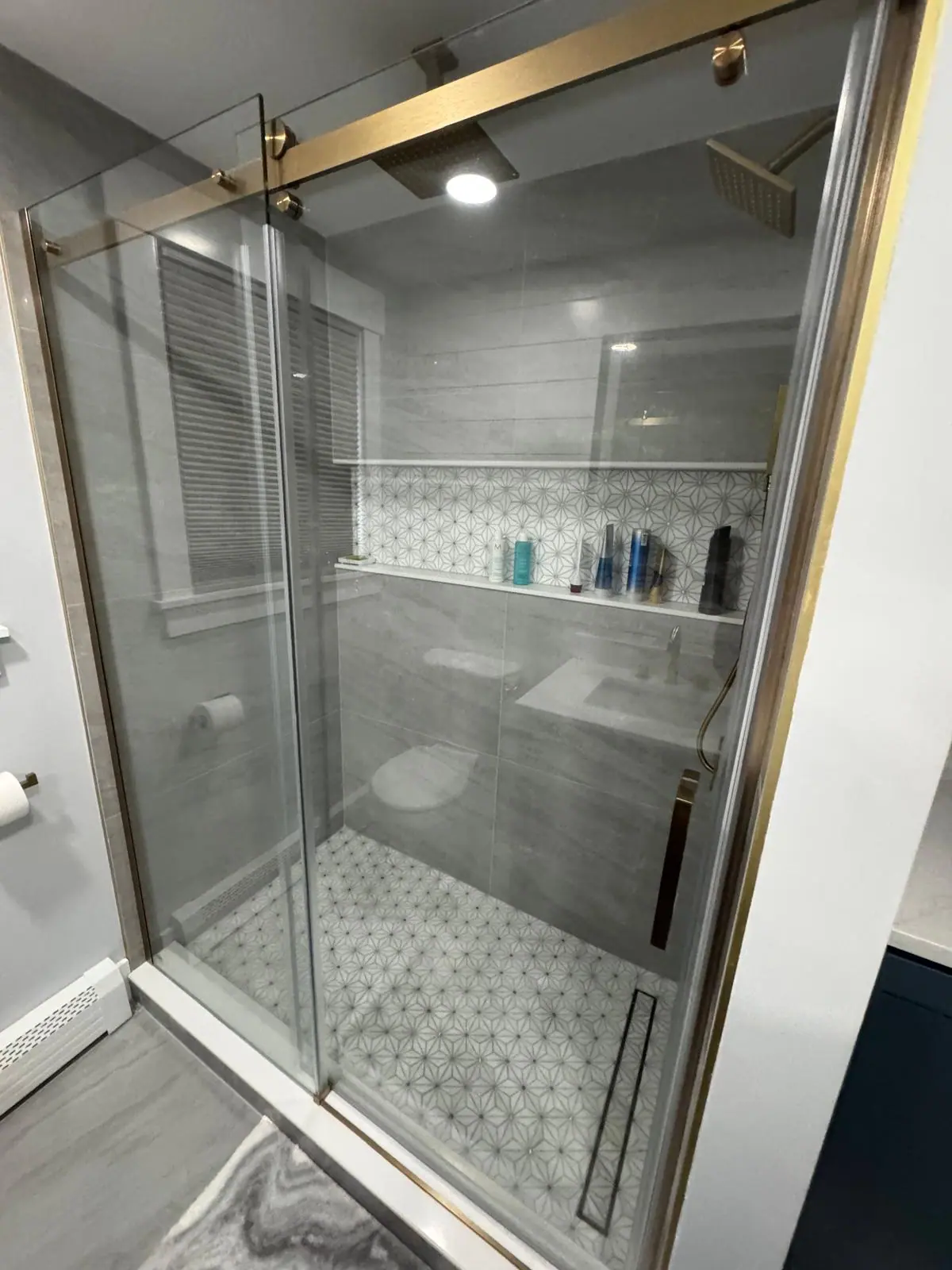 Glass shower with gray wall tile, a long shelf niche and a white star mosaic floor