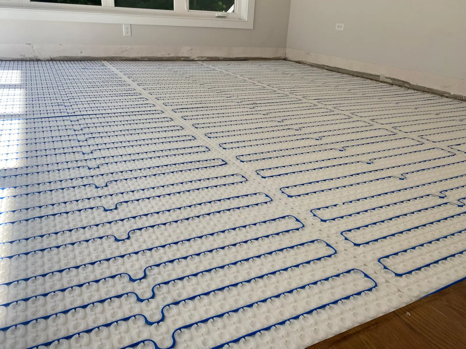 Blue radiant heating cable routed through a white studded membrane before tile installation