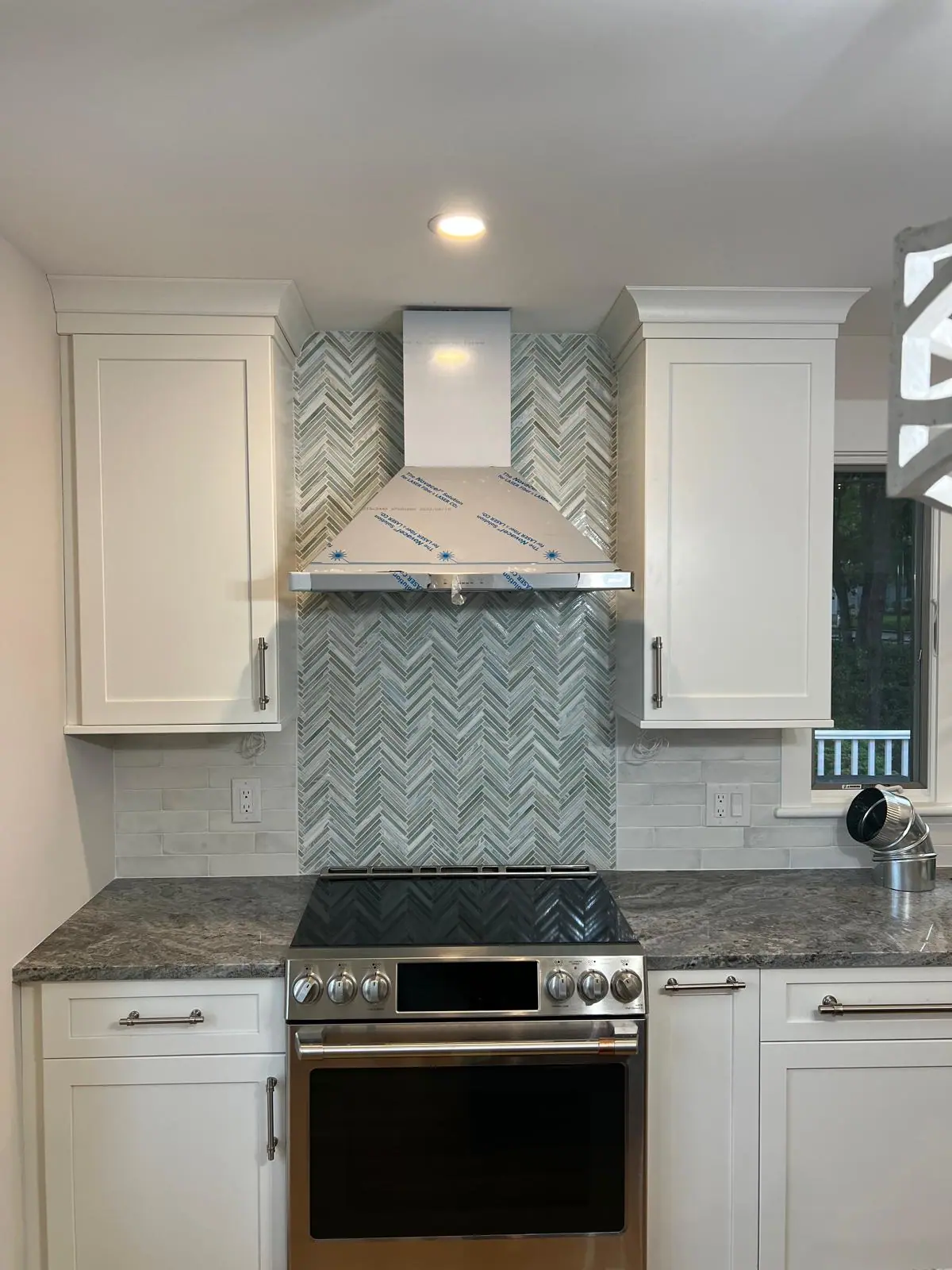 Blue-gray herringbone mosaic running from the counter to the ceiling behind a range hood, framed by white subway tile and white cabinets