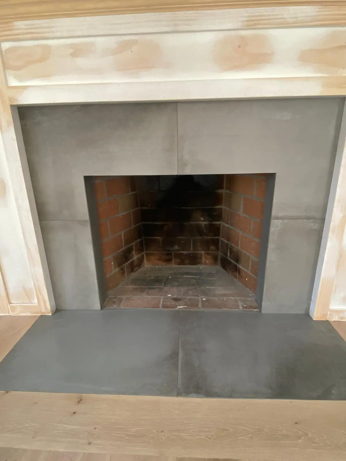 Fireplace surround and hearth in large-format gray porcelain tile, set inside a new wood mantel before painting