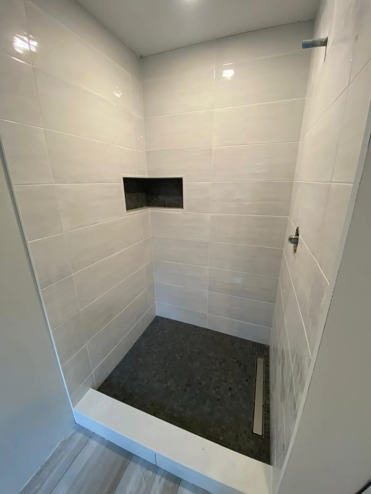 Shower in large white rectangular tile with a black niche and a dark mosaic floor