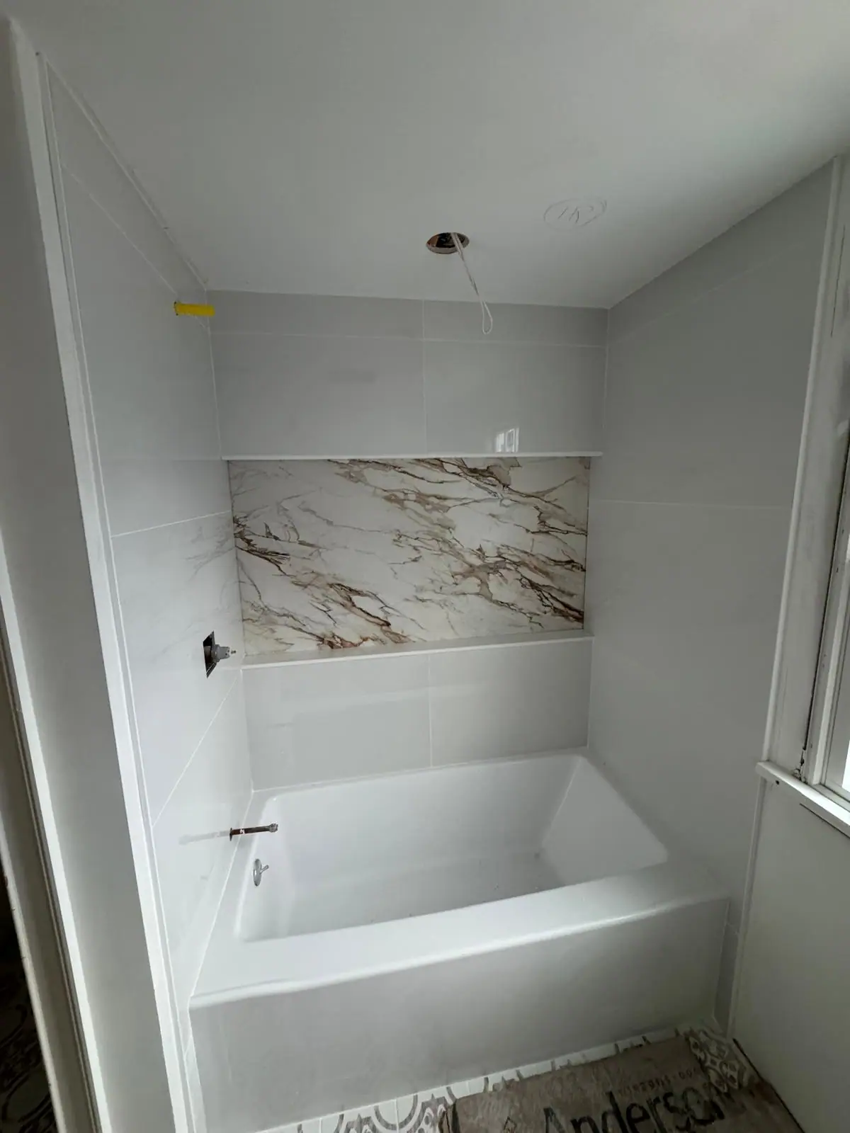 Tub surround in white tile with a wide marble-look accent band above the tub