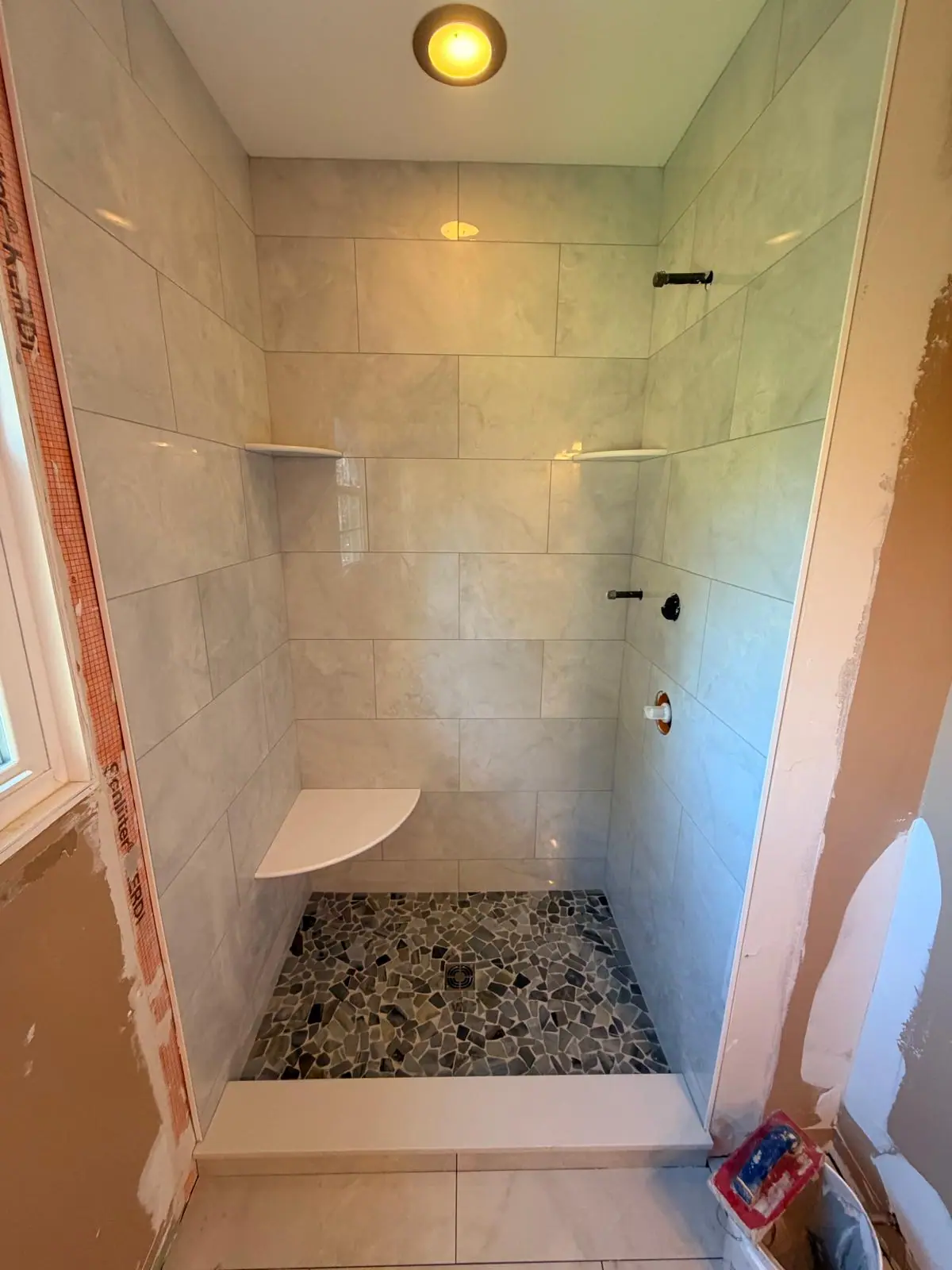 Marble-look tile shower with corner shelves and a pebble stone floor