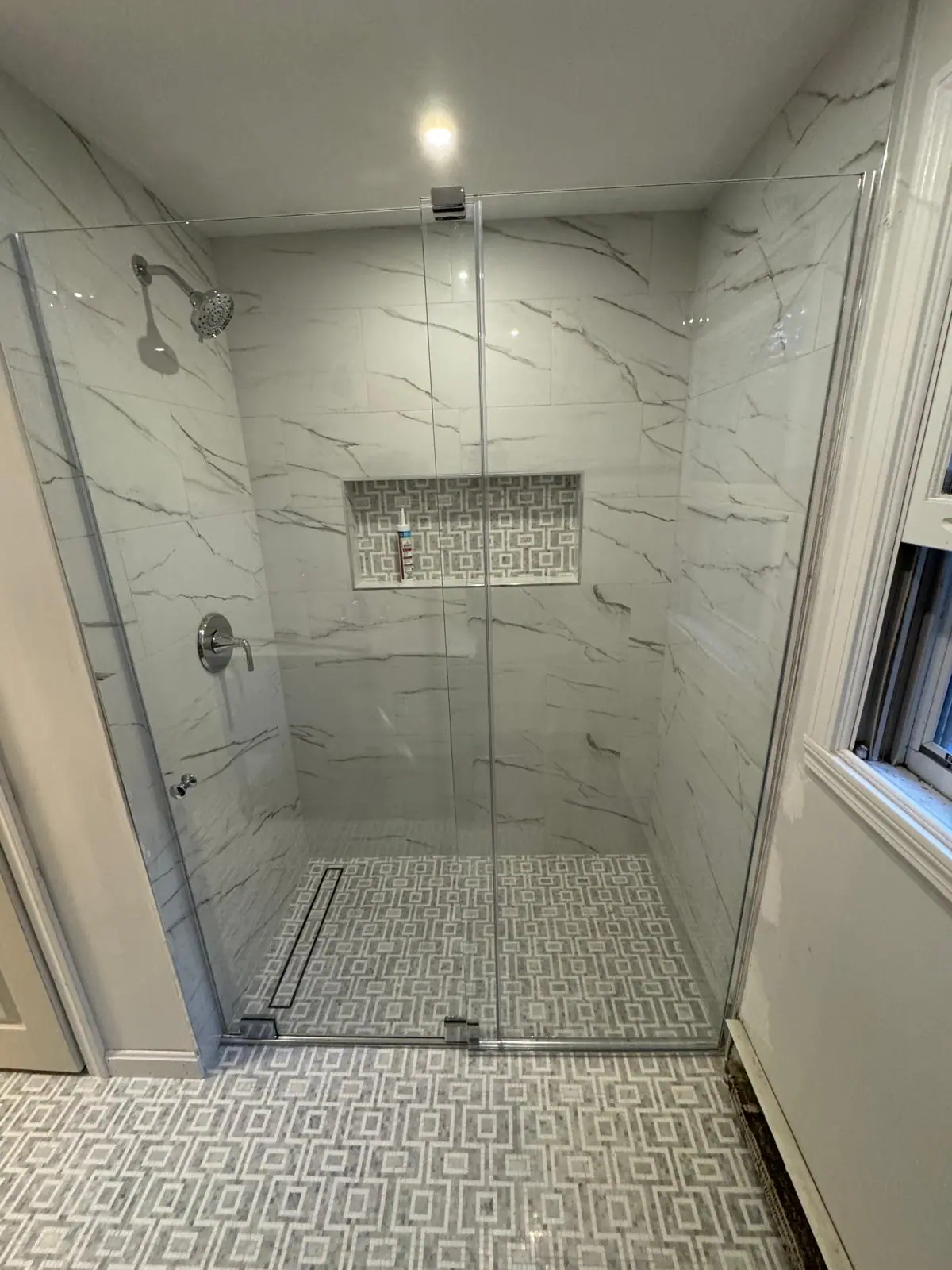 Glass shower with marble-look wall tile, a mosaic niche, a patterned floor and a linear drain