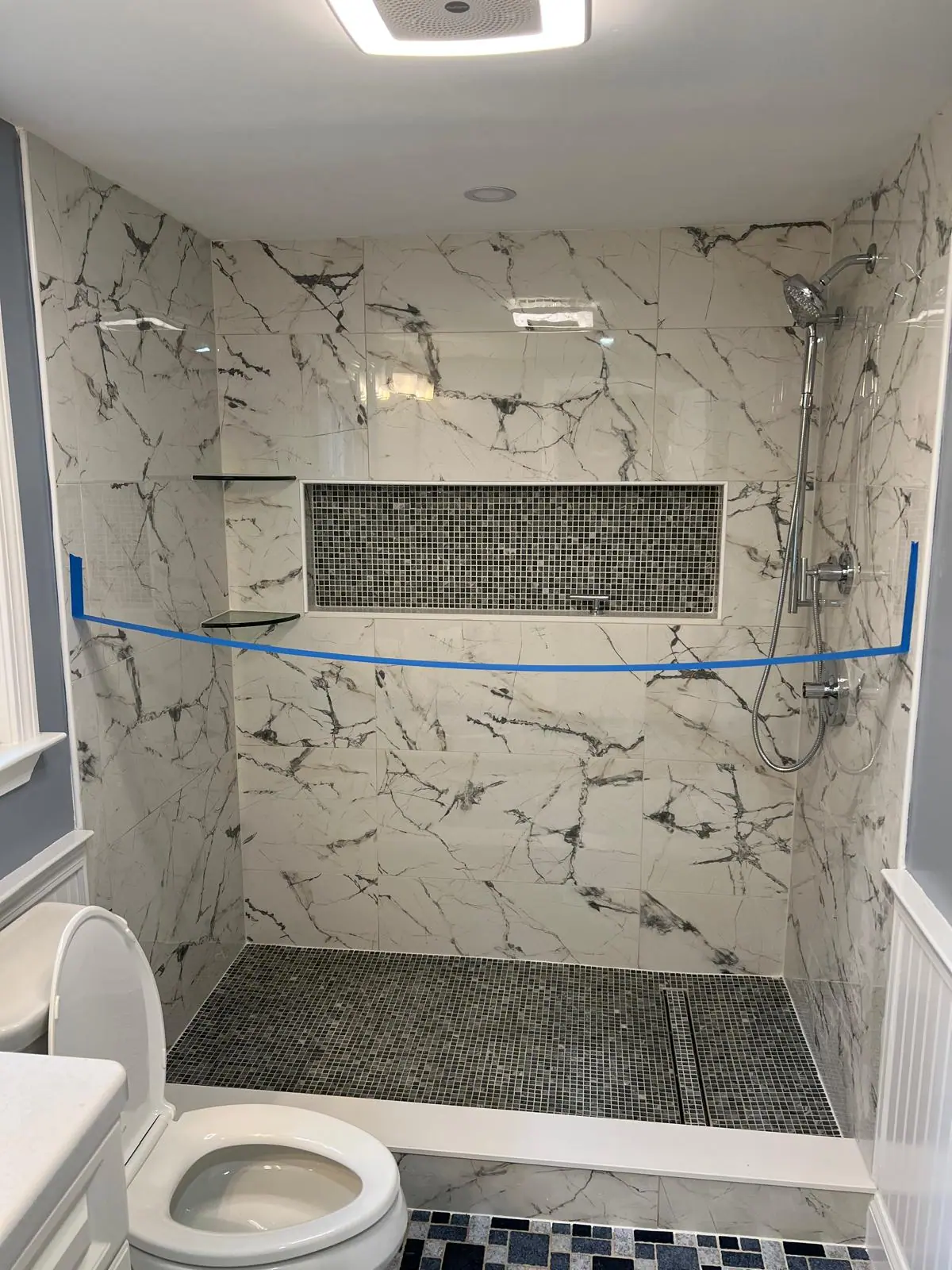 Marble-look shower walls with a long mosaic niche and corner shelves during installation