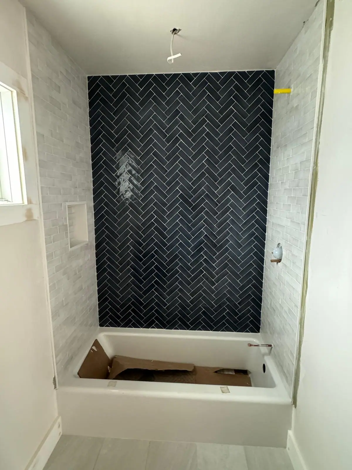 Navy herringbone tile feature wall above a new tub, with light gray tile on the side walls