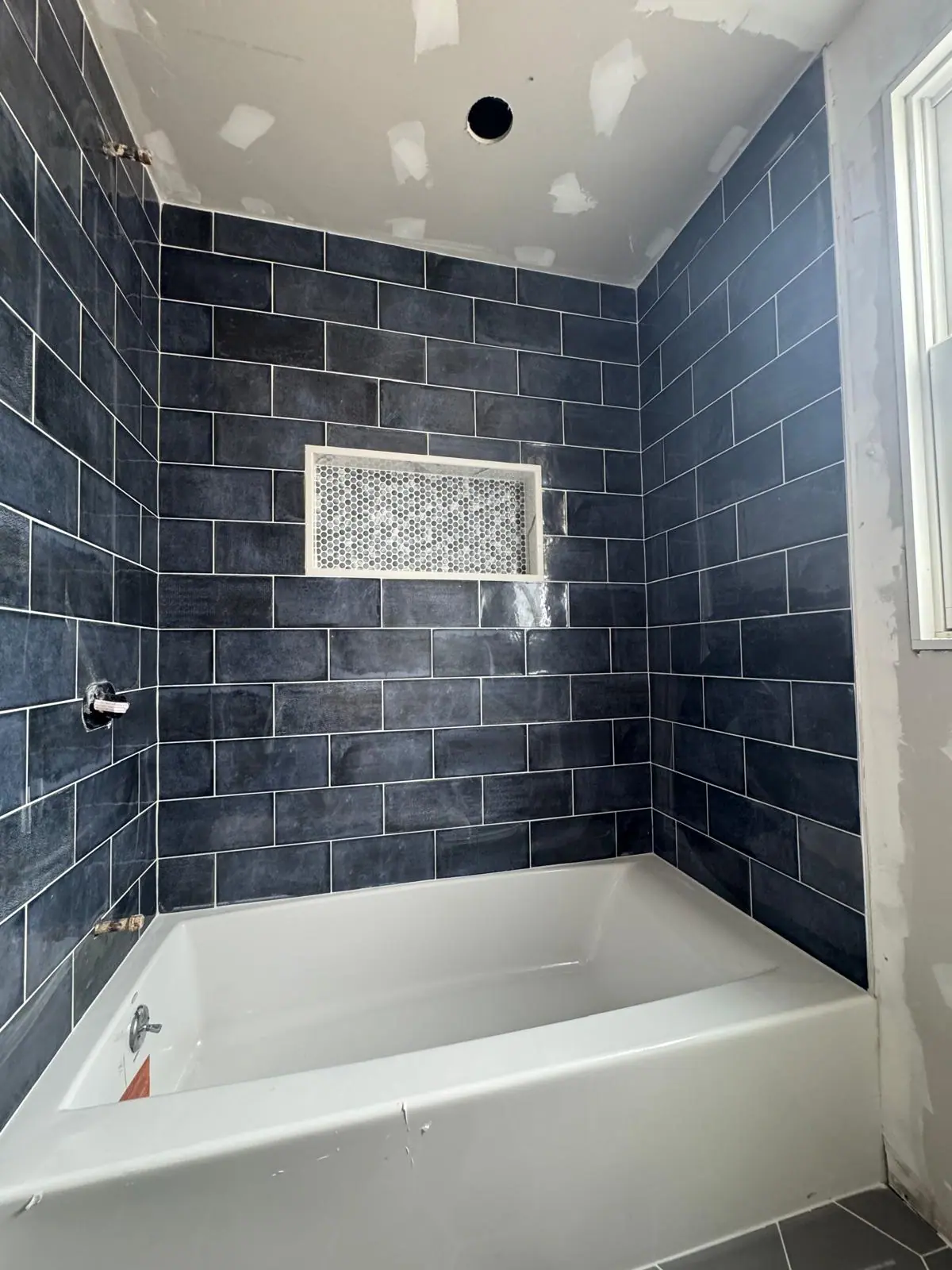 Tub surround in navy subway tile with a white framed niche and a mosaic insert