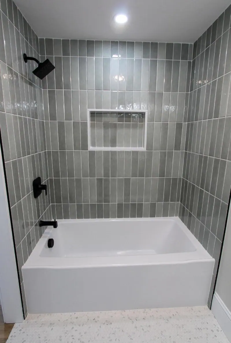 Tub surround in vertically stacked sage tile with a white niche and black fixtures