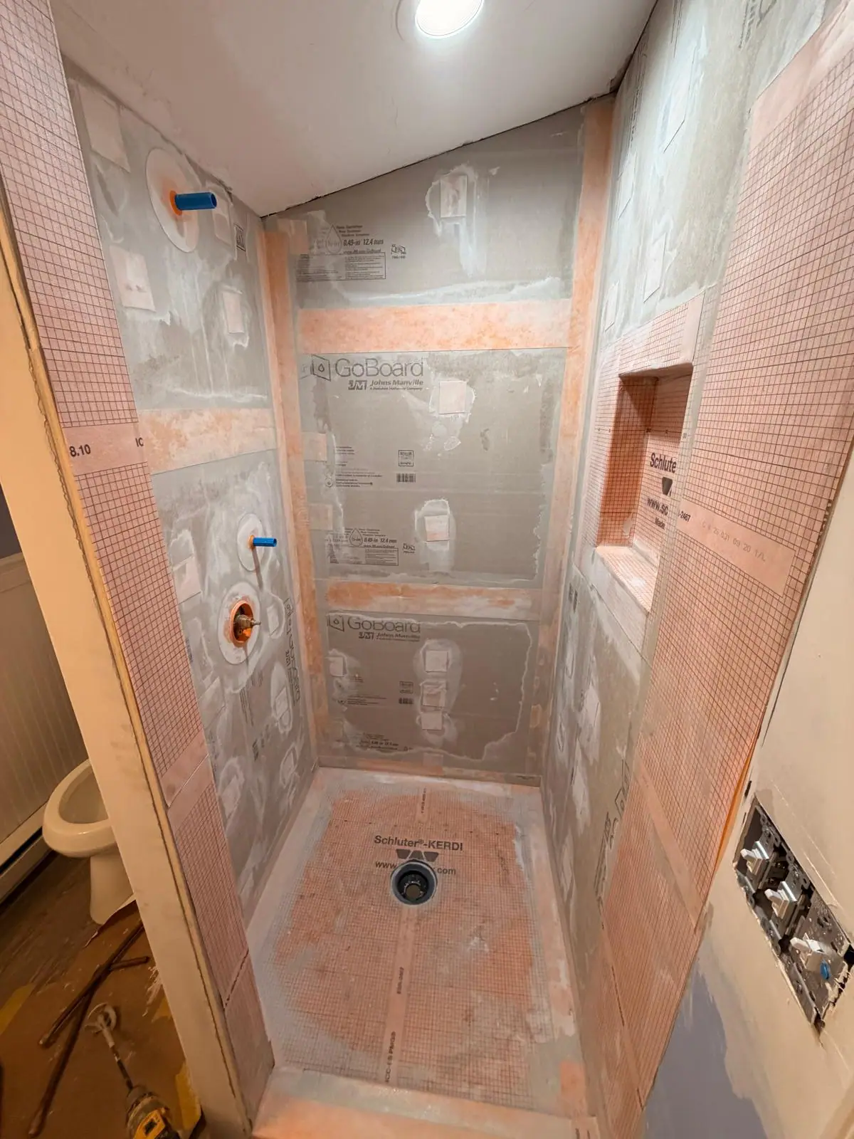 Shower walls, niche and pan covered in orange waterproofing membrane before tiling