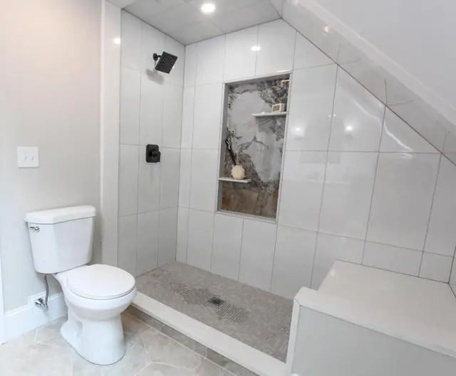 Shower under a sloped ceiling with large white tile and a marble-look niche