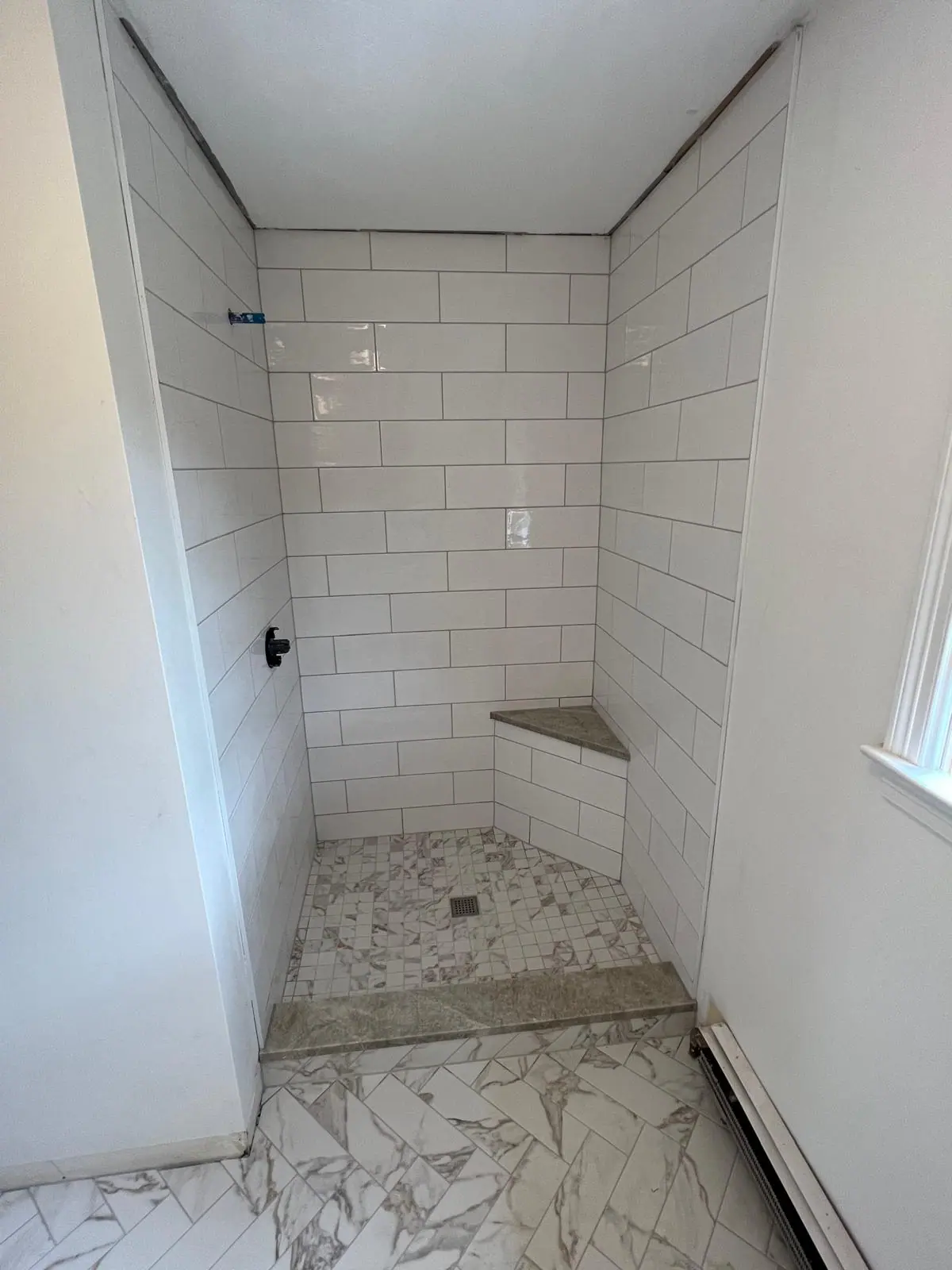 White subway tile shower with a corner bench and a marble-look mosaic floor