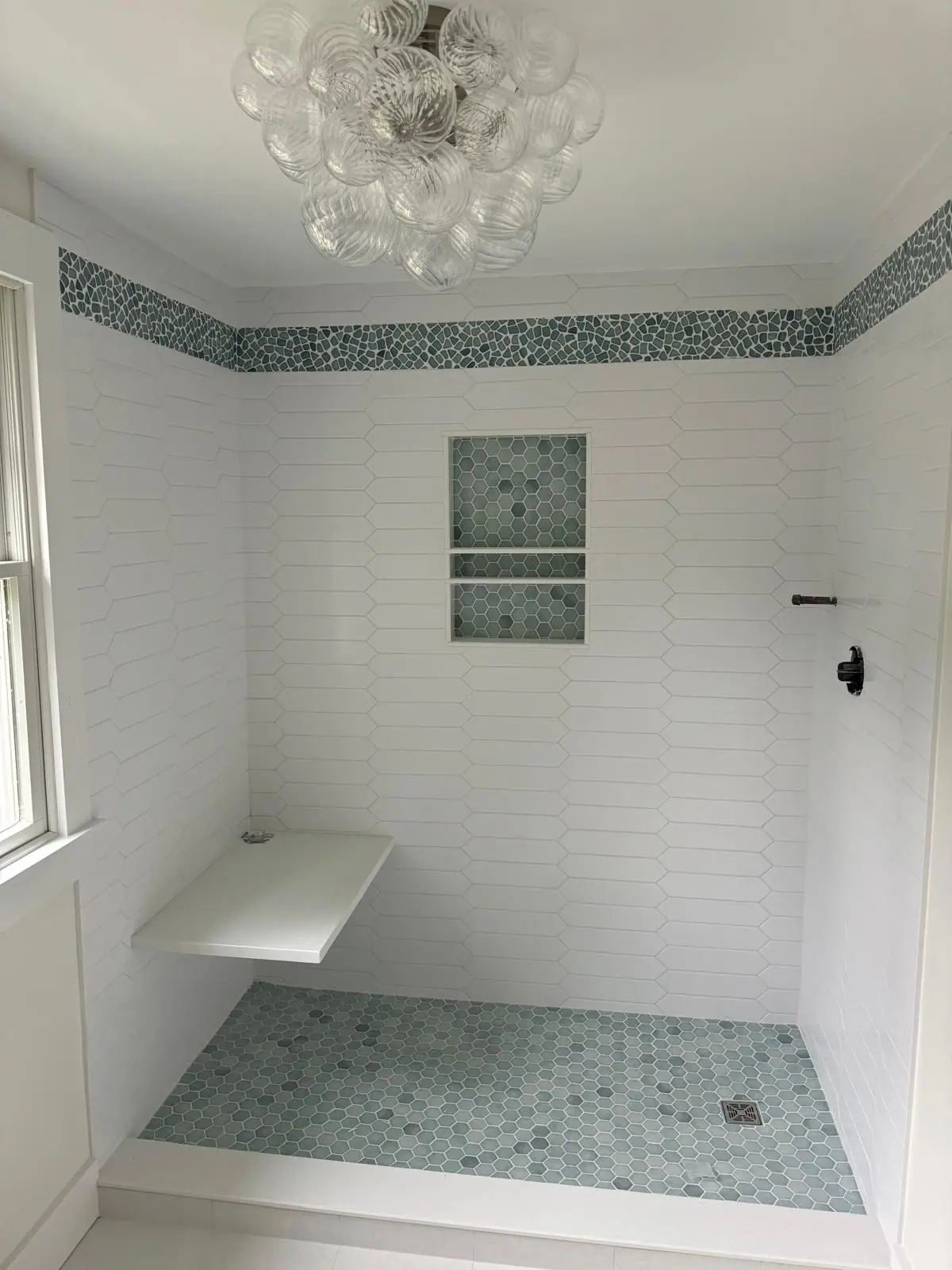 White subway tile shower with a green mosaic band, a mosaic niche and a floating bench
