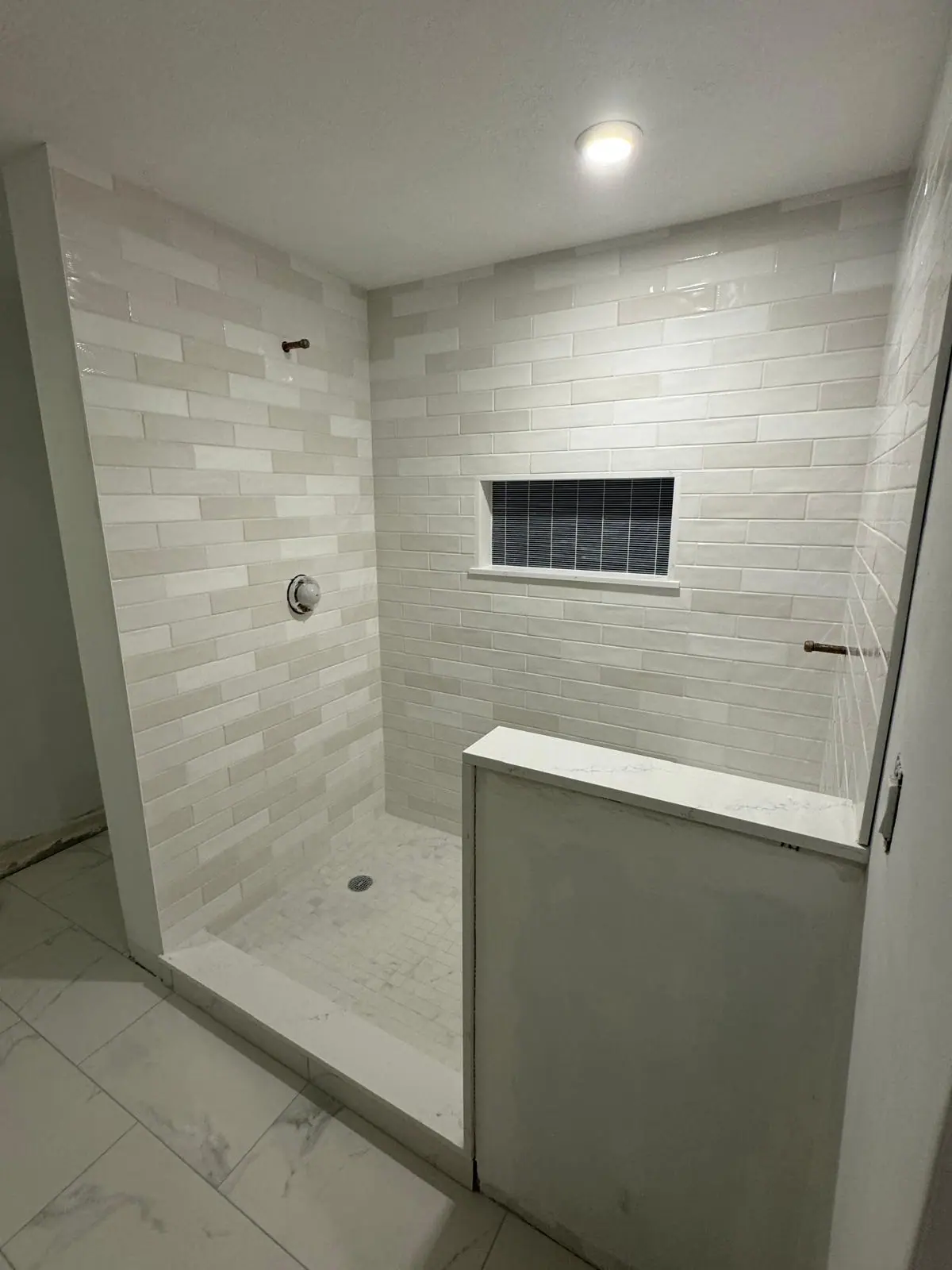 Light gray subway tile shower with a knee wall, a bench and a dark mosaic niche