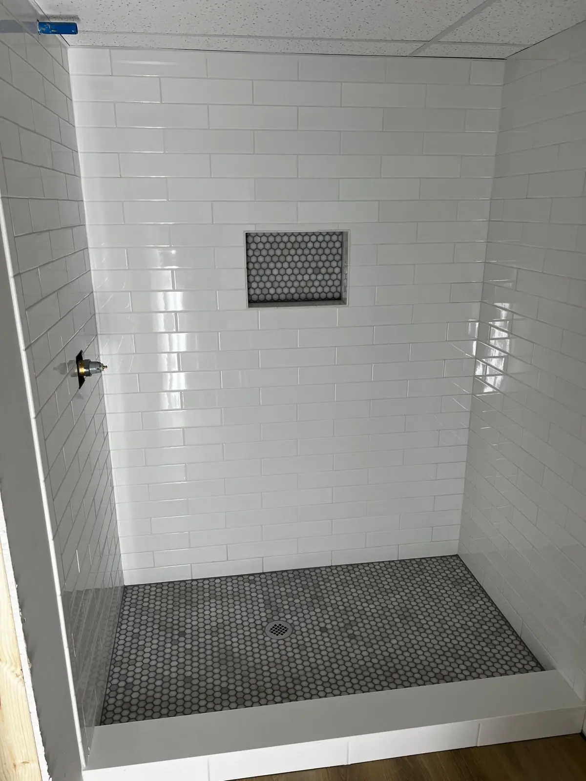 White subway tile shower with a hexagon mosaic niche and a gray penny tile floor