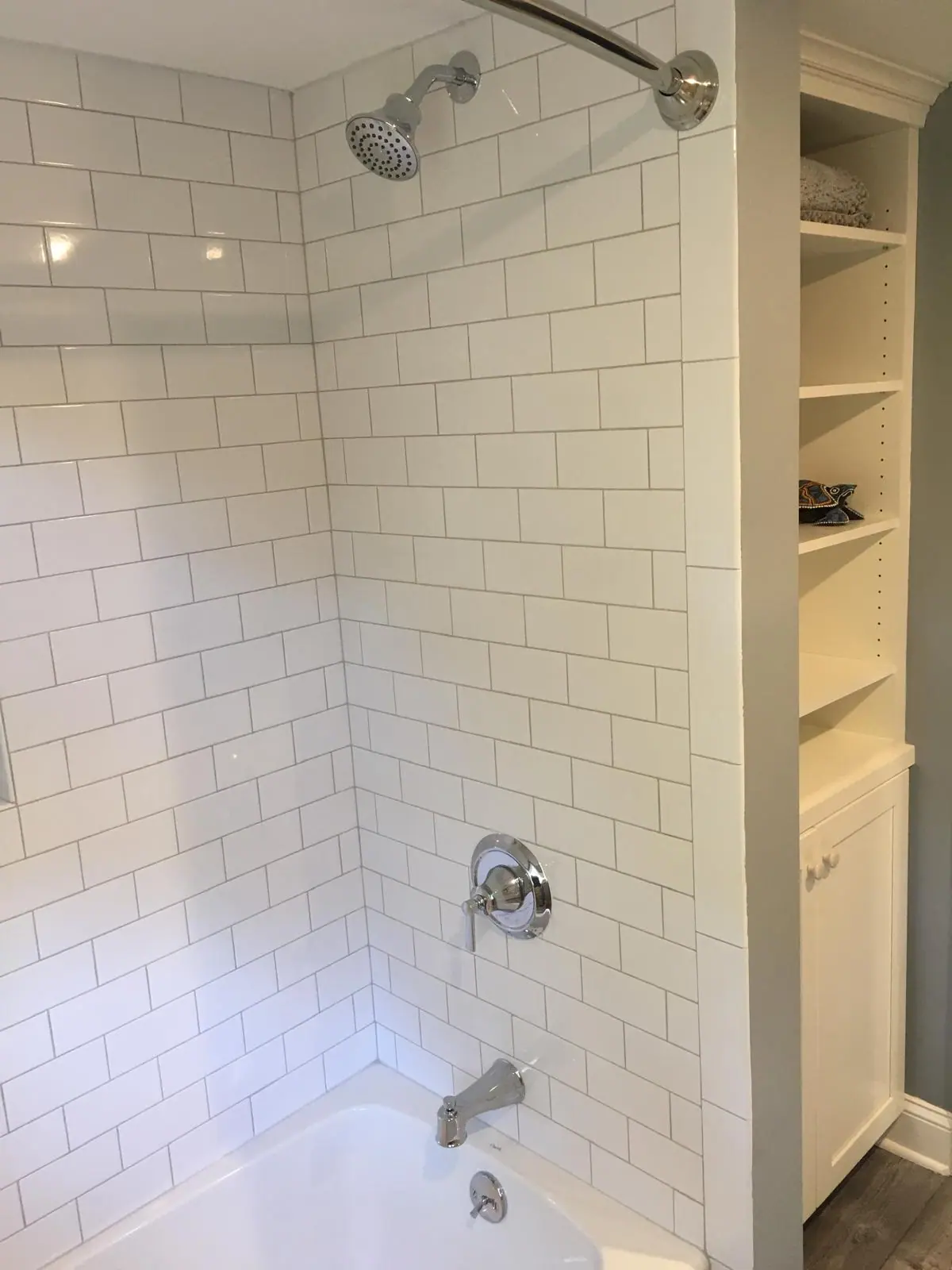 White subway tile tub surround with a chrome valve beside built-in shelving