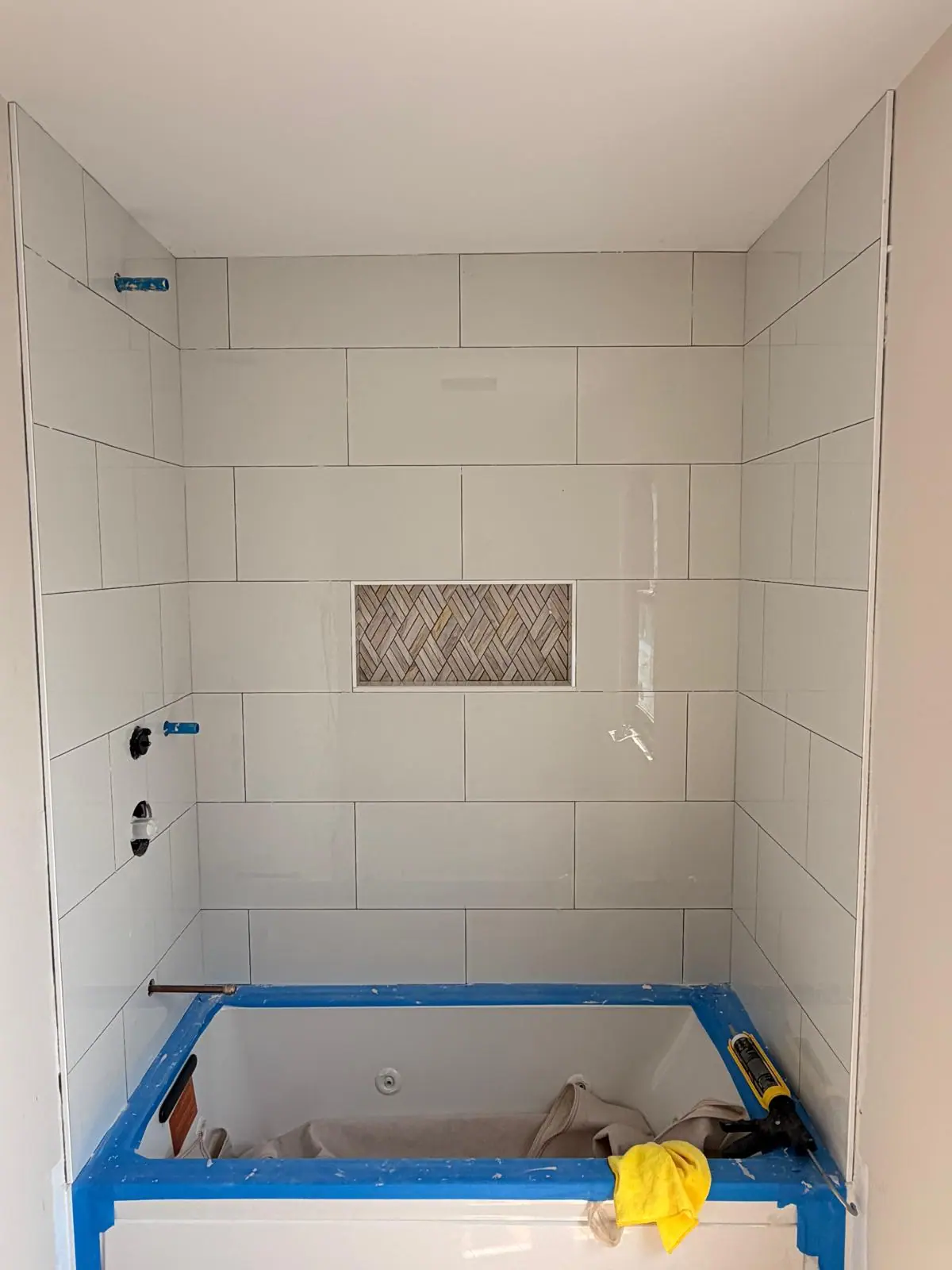 White tub surround with a herringbone tile niche, tub still protected during installation