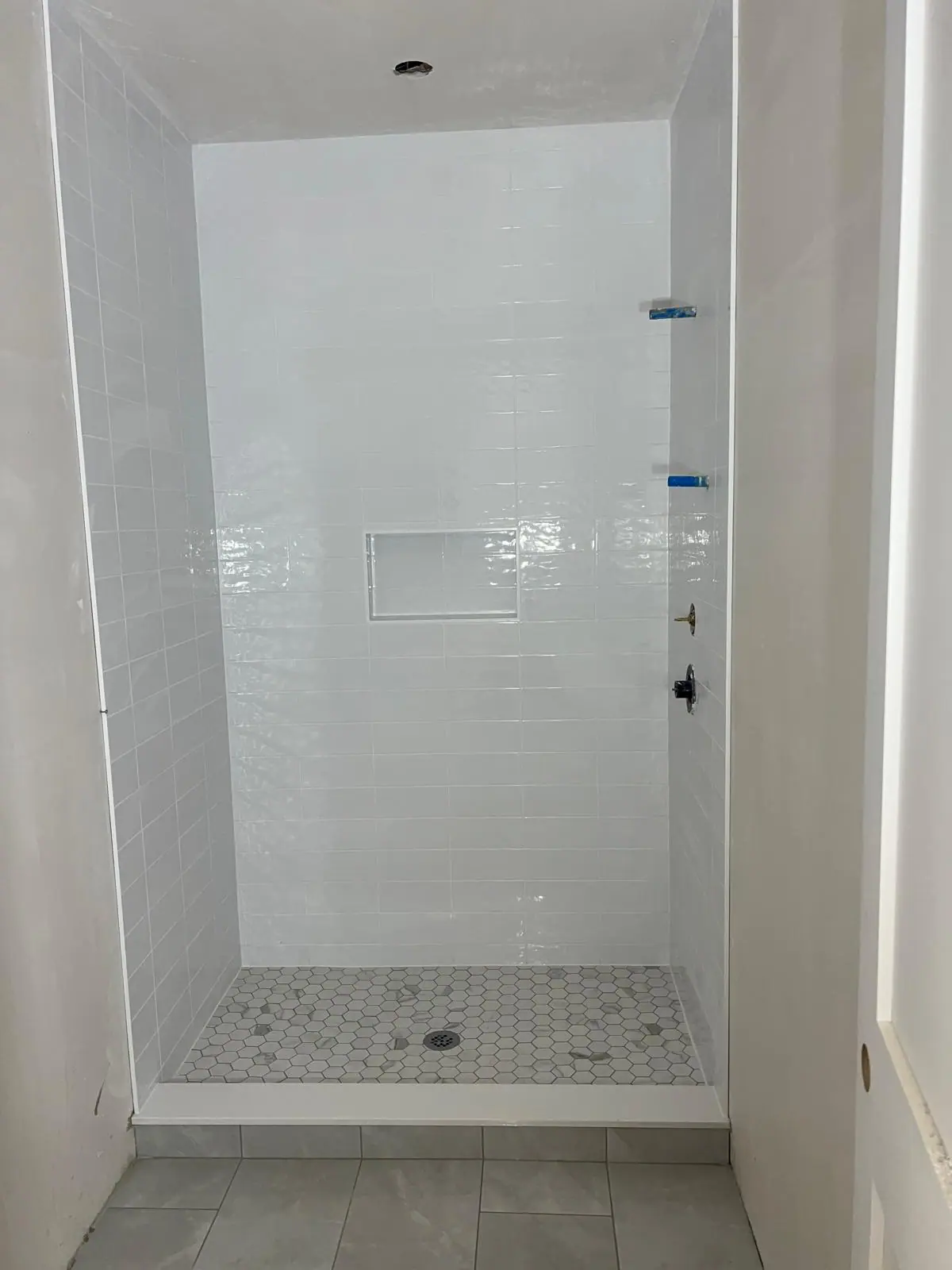 White tile shower with a framed niche and a gray hexagon mosaic floor