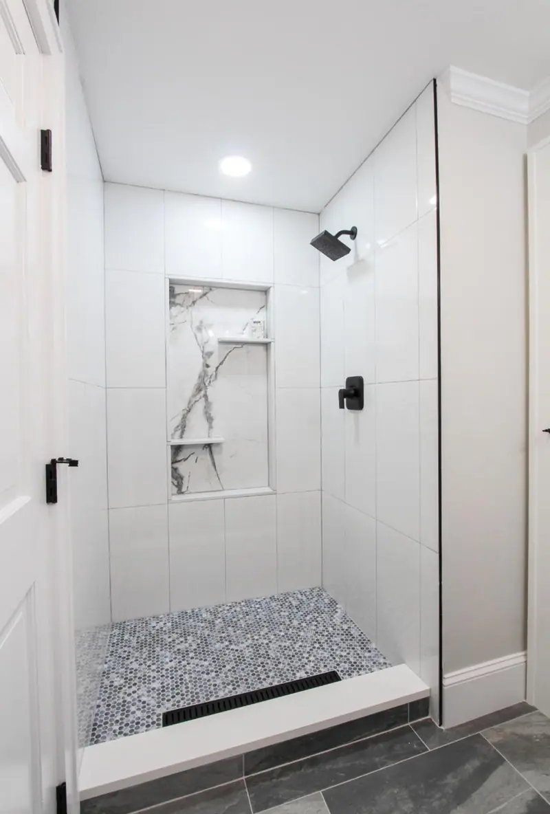 White tile shower with a marble-look double niche, black fixtures and a mosaic floor