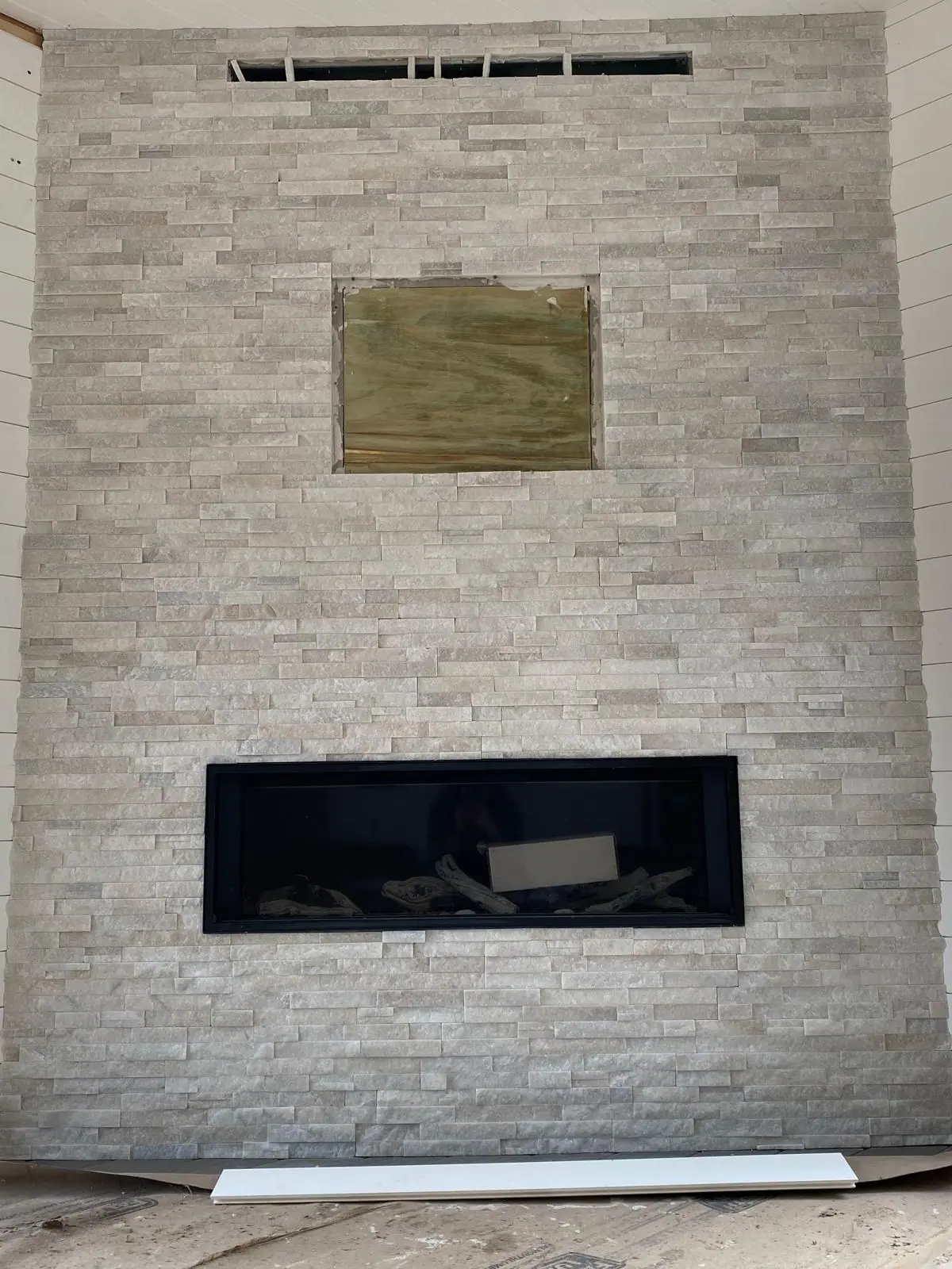 Full-height white stacked stone wall around a linear gas fireplace, with a recess left open above it during installation