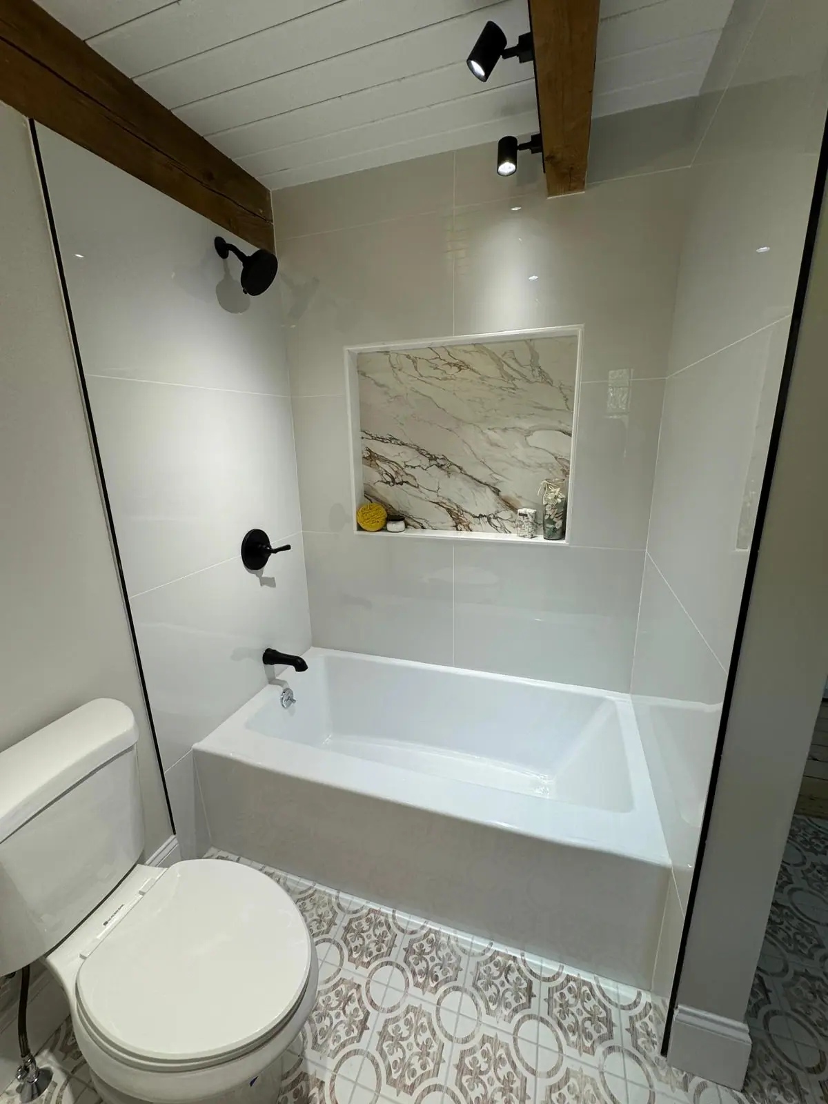 White tile tub surround with a marble-look niche and black fixtures