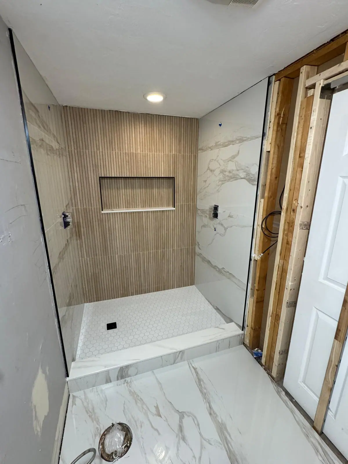 Shower with a vertical wood-look accent wall, a long niche and marble-look side walls