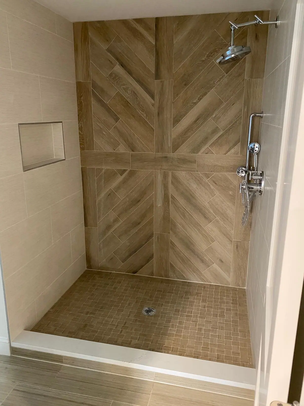 Walk-in shower with a wood-look tile wall in a chevron pattern, a recessed niche and a mosaic floor